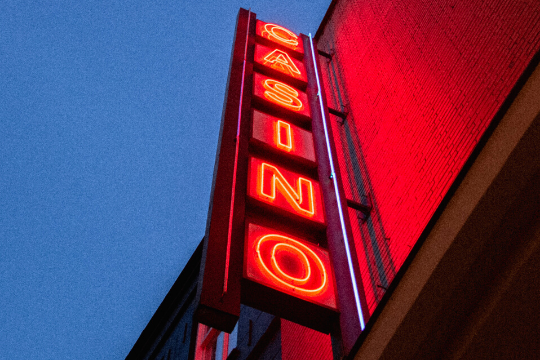 A vertical neon sign glows red with the word CASINO against a blue evening sky, mounted on the side of a red brick building.