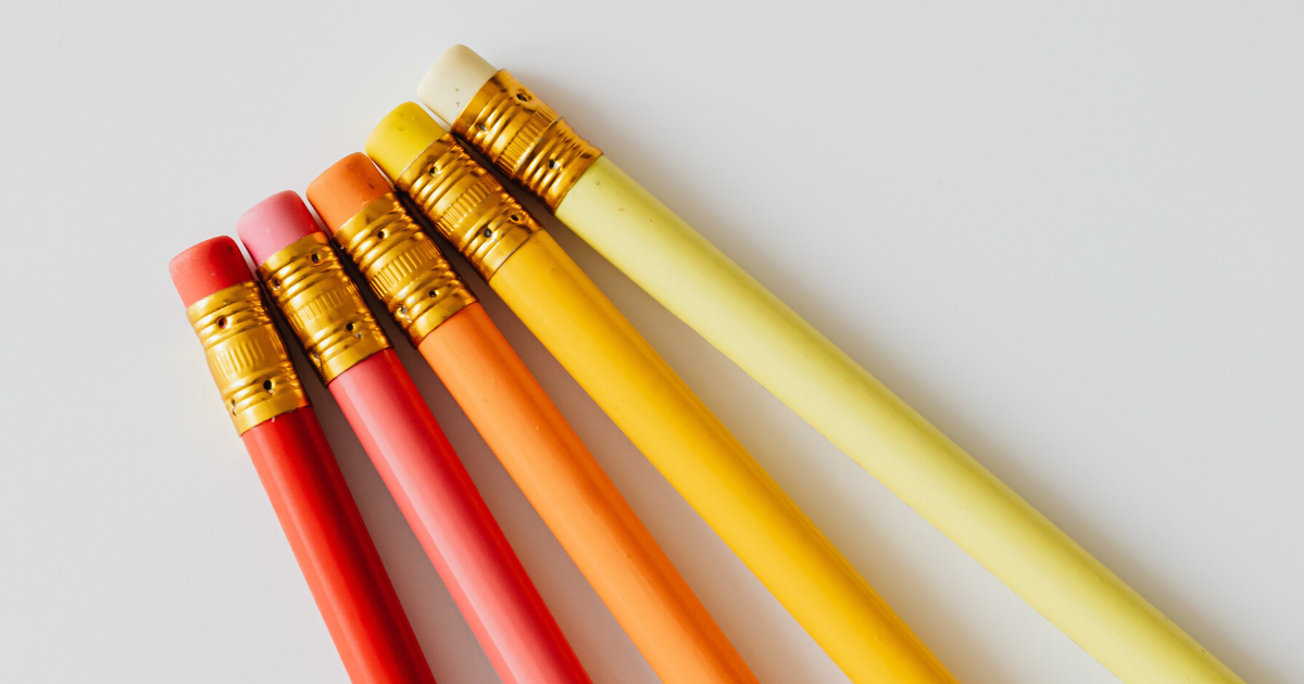 A close-up of five pencils and erasers arranged in a gradient from pink, to orange, to yellow