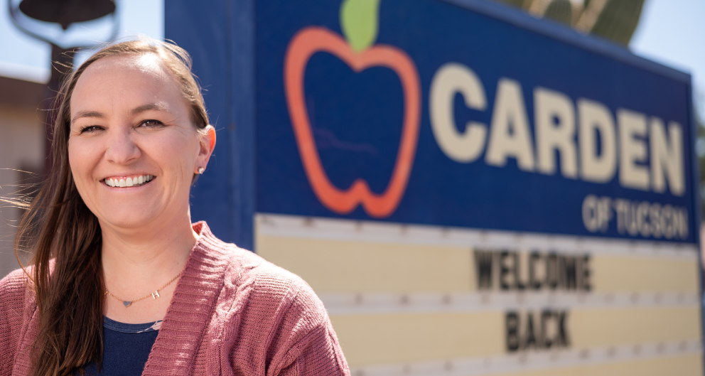 Katy Martinez, teacher and office manager for Carden of Tucson, stands smiling in front of the Carden sign.