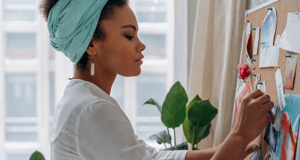 A young woman pins images onto a cork board to visualize goals
