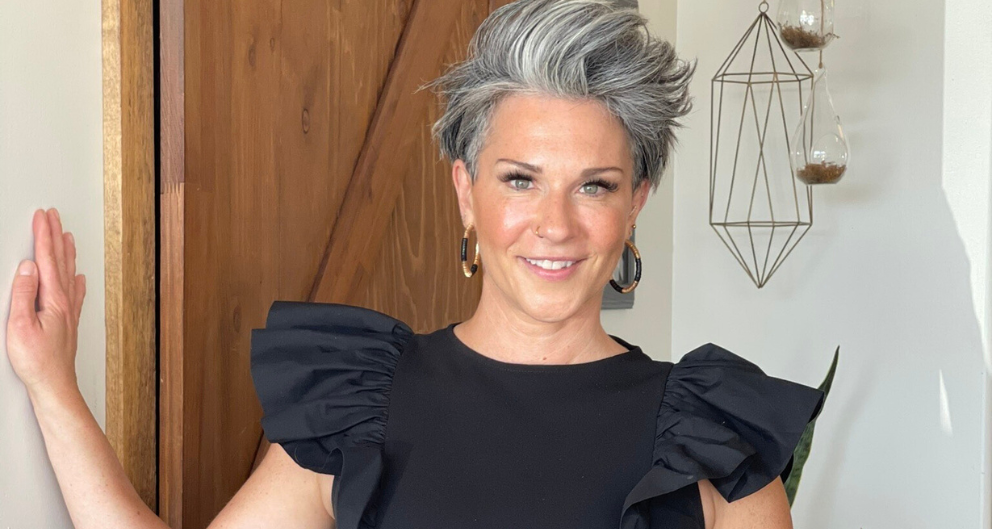 A close up shot of Jenna Speight, a smiling woman with spiky gray hair wearing a black blouse and chunky earrings.